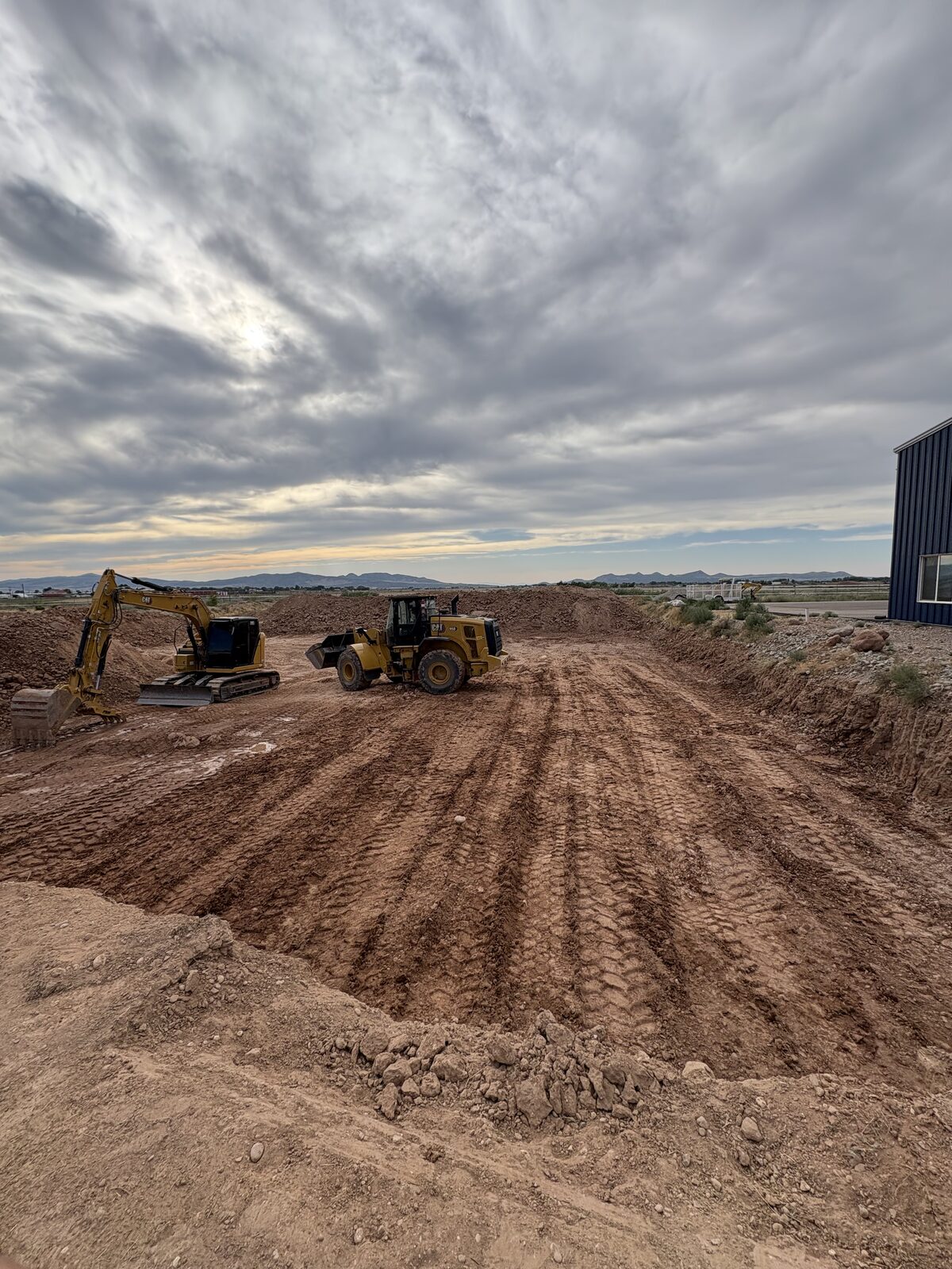 Roxor South excavator and wheel loader rough-grading at dusk in Kane County, Utah