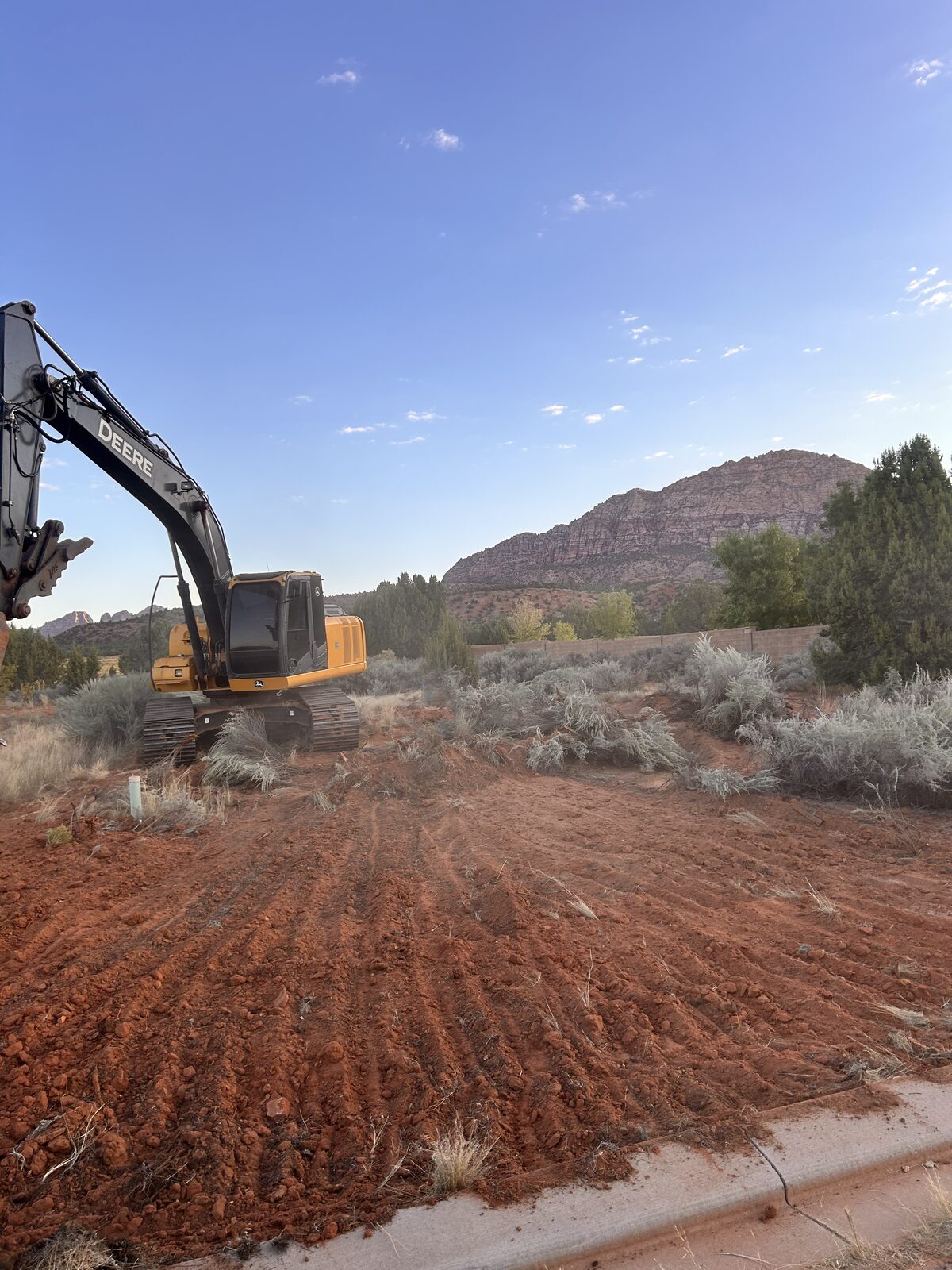 Roxor South Deere excavator finishing a custom-home yard in Ivins, Utah with the Red Mountain behind